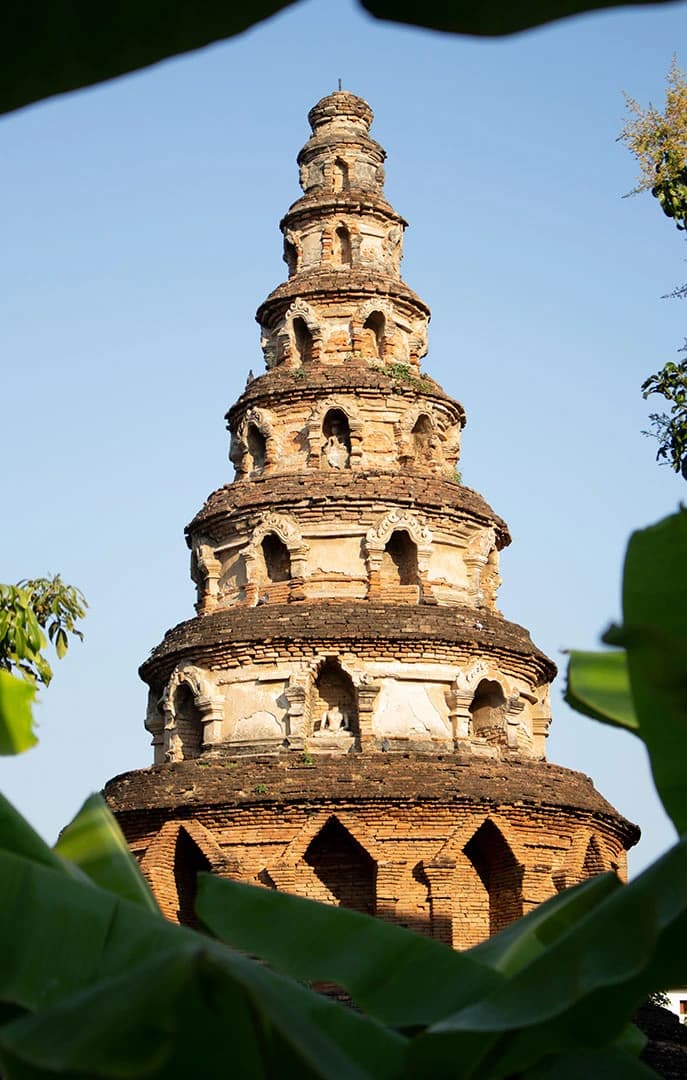 una torre a Chiang Mai (Thailandia). La torre ha una forma conica realizzata in mattoni ed è circondata da molte piante verdi, che coprono la parte inferiore della torre