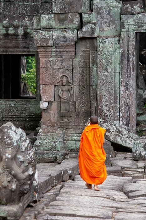 un giovane monaco che cammina in un tempio vicino ad Angkor Wat (Cambogia). Il monaco indossa una veste arancione tradizionale