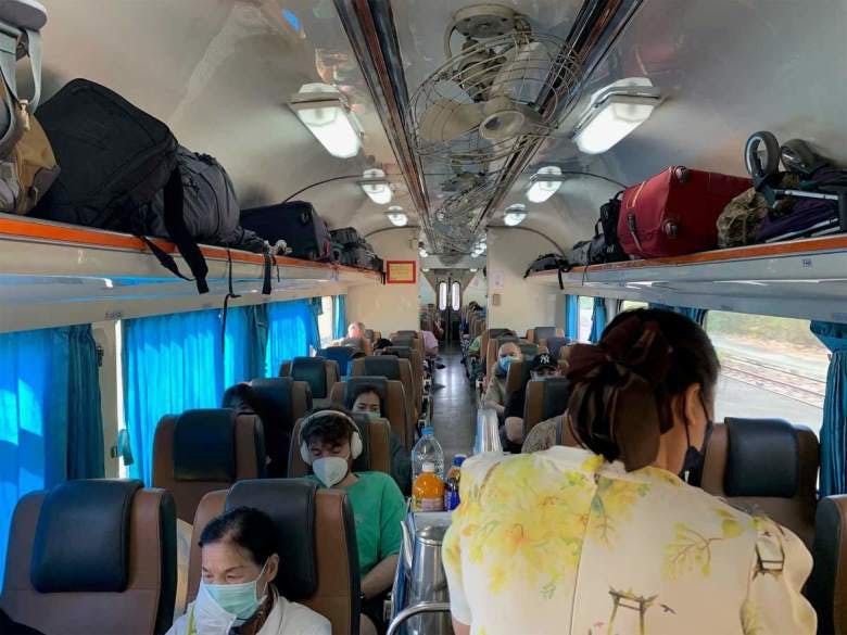 Photo of our carriage on the way to Chiang Mai. In the second row you can spot Davide with his heapdhones on, wearing a green shirt and also wearing a mask. On the both sides there are a lot of luggages in the top on the train. In the front there is a woman from the crew who is dealing meals to the passengers
