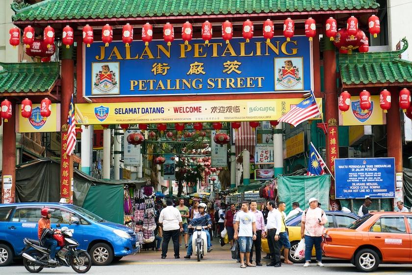 Ingresso di Chinatown, Kuala Lumpur. Nella foto spicca il tradizionale arco con architettura cinese. L'arco è di colore rosso, con il tetto colorato di verde. Intorno al bordo del soffitto sono appese molte lanterne cinesi., anch'esse di colore rosso.  Sotto l'arco ci sono molte persone, di varie etnie.