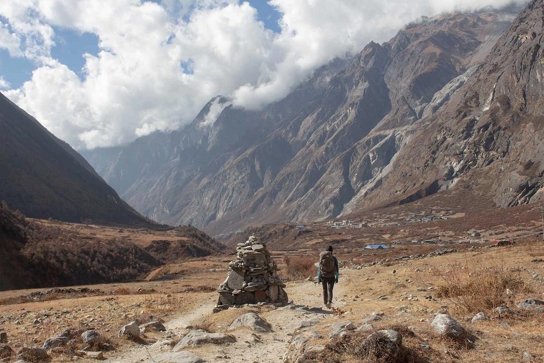 Between Langtang village and Kyanjin Gumpa the valley looks vast. Pauline is ahead of me walking next to the Mani stone wall, there are clouds in the sky.