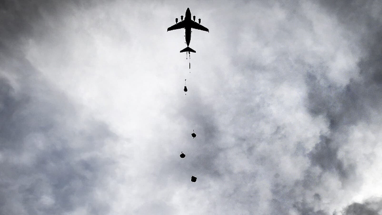 missing image In alto, orizzontalmente al centro, si trova un aereo da caccia che sta sganciando bombe. Il cielo è coperto da nuvole scure. La foto è in bianco e nero.