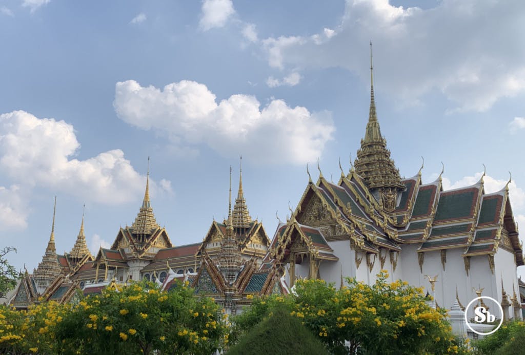 Vista del complesso del palazzo reale di Bangkok. Nella foto si intravedono principalmente i tetti dei vari edifici. Tutti i tetti hanno la tipica struttura thailandese con "trinagoli crescenti" e sono decorati con bordi oro e rossi e la parte centrale colorata di verde smeraldo. In cima ad ogni tetto è possibile ammirare una stupa di colore oro.