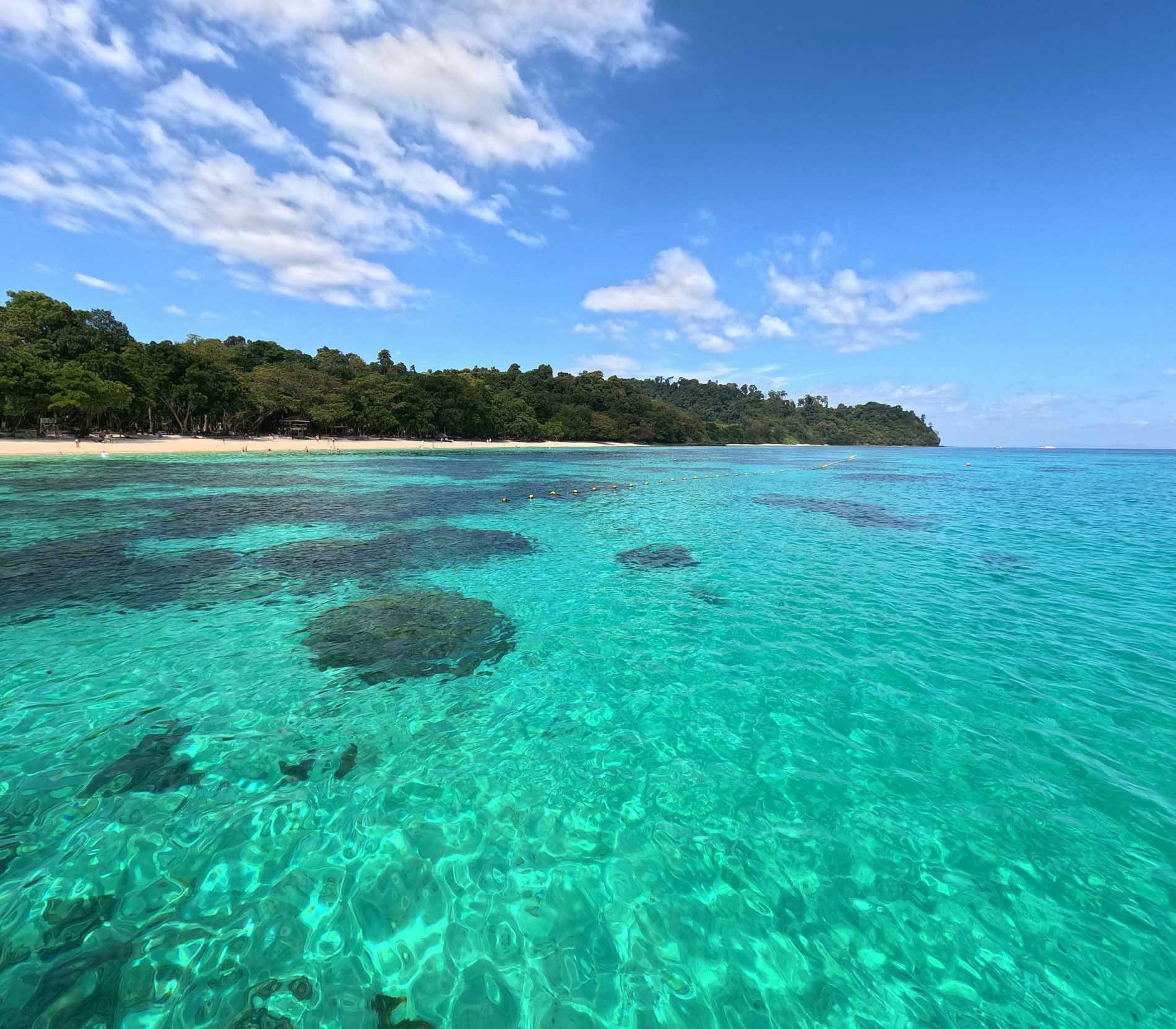 Sea water and view of white sandy beach with jungle in the background at Koh Rok, an island in the Gulf of Thailand.